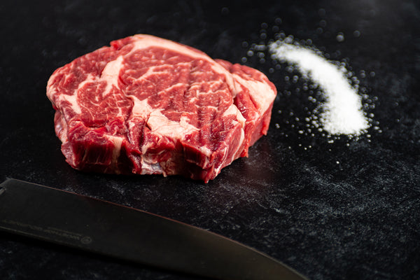 Thick cut delmonico steak from BetterFed Beef pictured with coarse sea salt. Highly-marbled and very tender, this steak is an affordable alternative to the ribeye