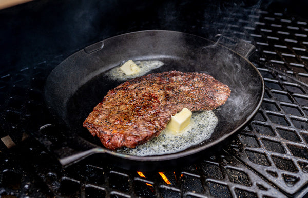 A Certified ONYA® flat iron steak searing in butter in a cast iron pan on a grill. 