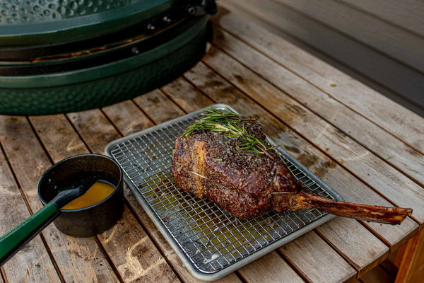 Impressive Certified ONYA® Tomahawk Ribeye Steak from BetterFed Beef rests with compound butter on a drying rack after being seared at high heat on a Big Green Egg charcoal grill. 