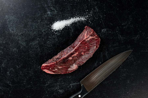 A Certified ONYA® beef hanger steak also known as a hanging tender and a butcher's steak photographed with sea salt and a chef's knife. This American steak is one of the best steaks available for sale online and is as tender as wagyu