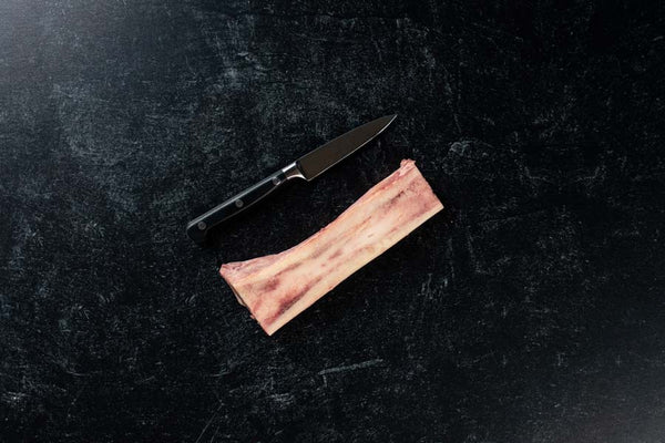 Beef bone marrow from BetterFed Beef for sale online. The 6 inch bone is split in half canoe cut style and is photographed next to a sharp knife