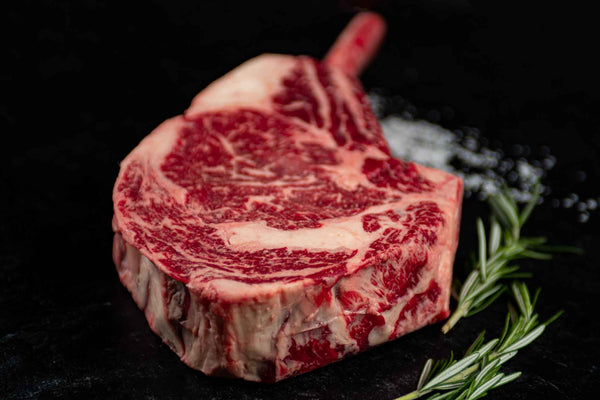 Certified ONYA® Tomahawk Ribeye photographed raw with beautiful marbling. Shown with garnishes including sea salt and rosemary