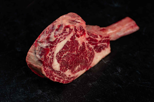 Side profile photo of a Certified ONYA® Tomahawk Ribeye with abundant marbling and as tender as Wagyu beef. Three inches thick with an exposed bone handle
