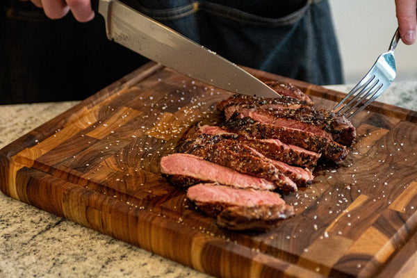 A home chef slices a Certified ONYA® Ribeye steak from BetterFed Beef on a wooden cutting board on a granite countertop in his modern kitchen. This steak is as tender as wagyu and highly marbled