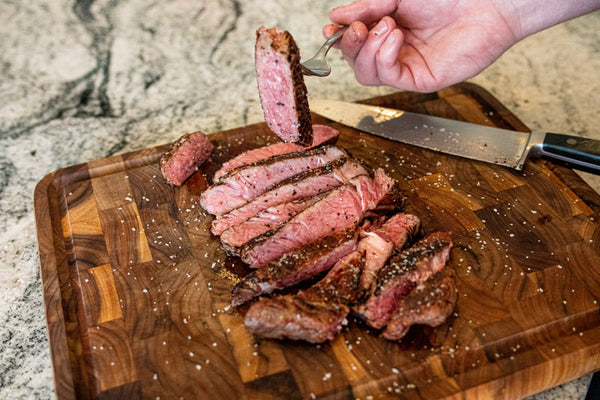 A medium rare Certified ONYA® Ribeye steak from BetterFed Beef sliced on a cutting board. A piece of the super tender steak can be seen on a fork about to be eaten by the home chef and his guests 