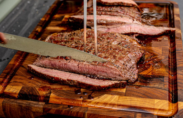 A perfectly cooked Certified ONYA® flank steak cut against the grain with a Wusthof chef's knife on a wooden cutting board. A home chef prepares this steak to host family and friends